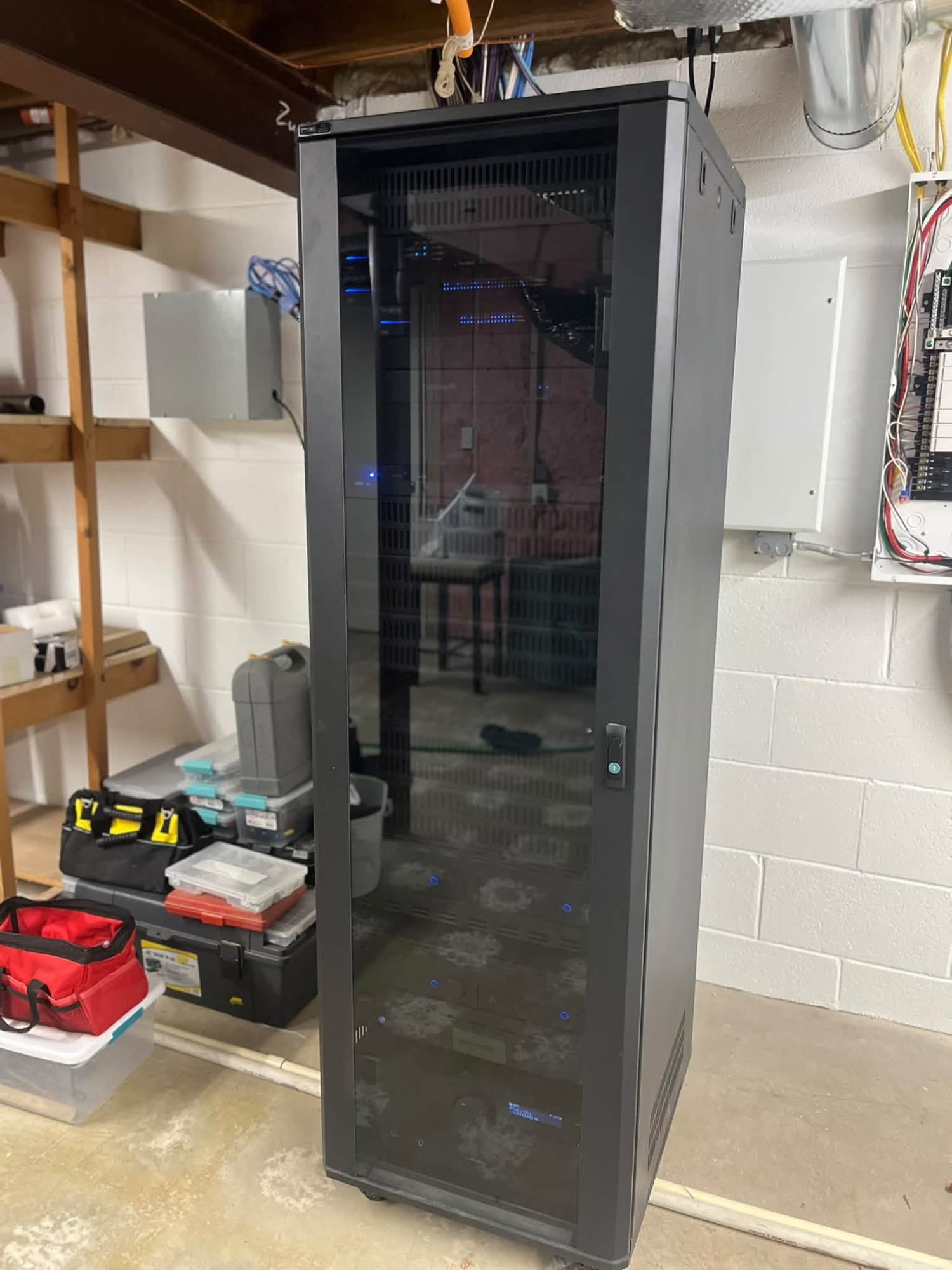 A black equipment rack cabinet standing in an unfinished basement before the wall goes up around it