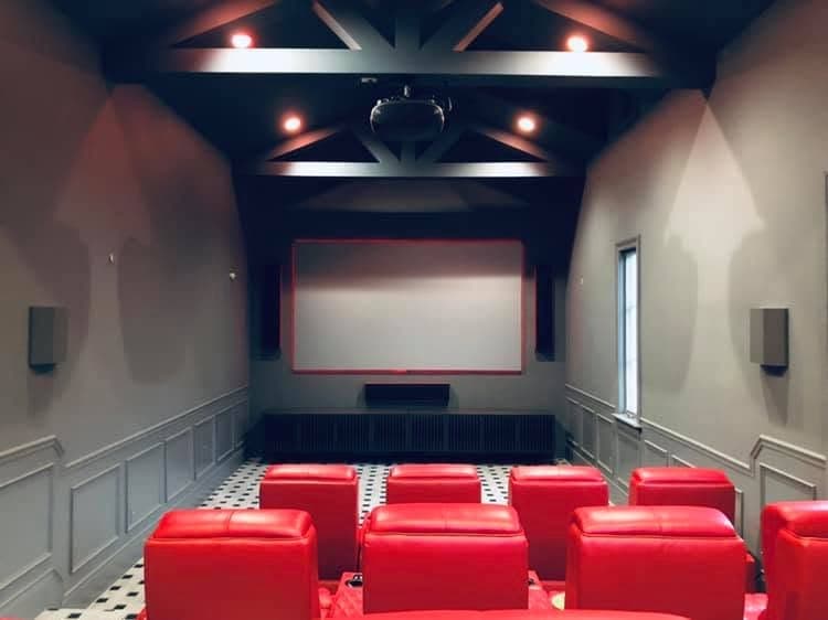 A private bowling alley converted into a home theater, with red leather seating, a black beamed ceiling, and a red-trimmed screen