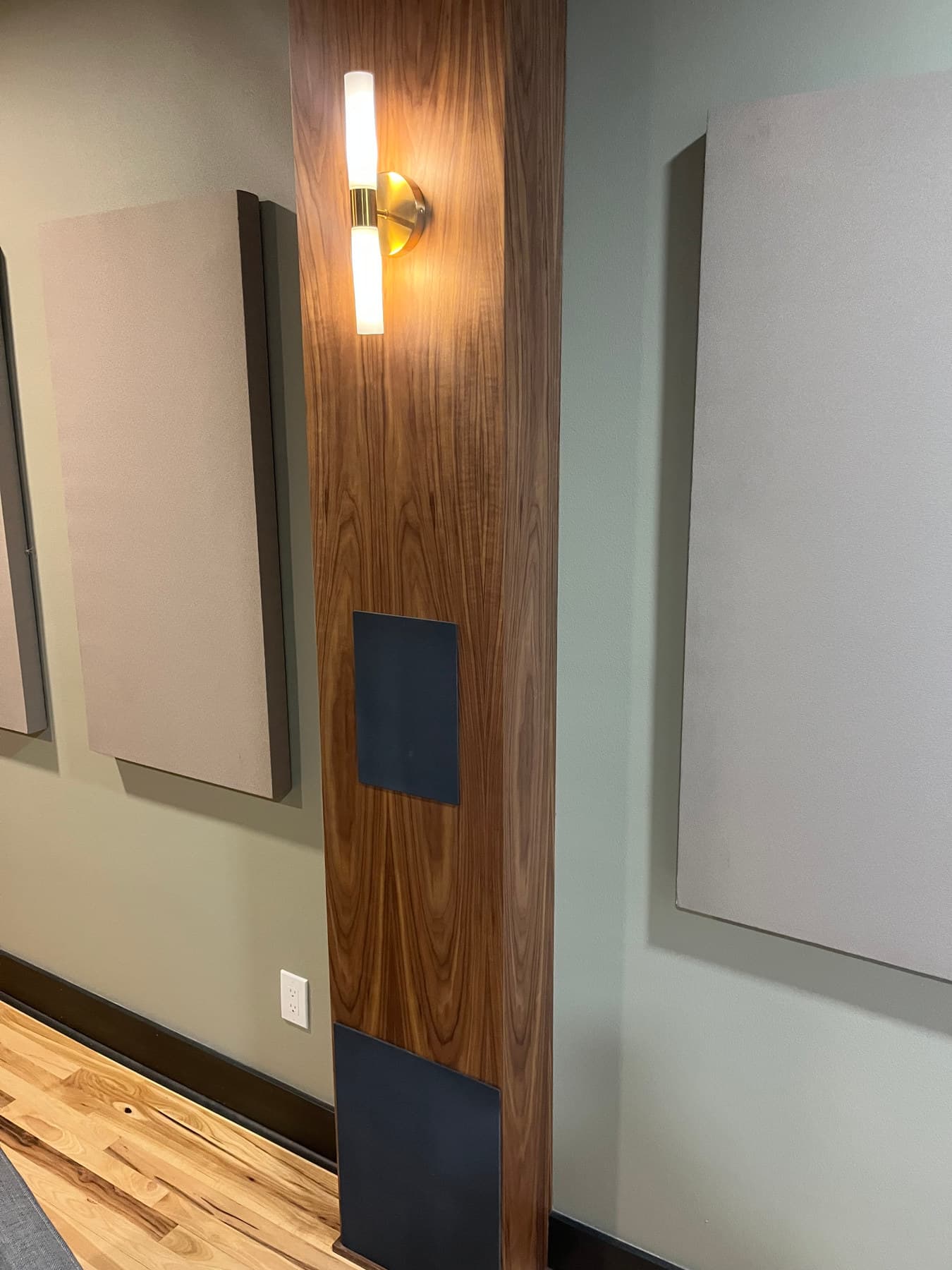 A walnut column with a concealed speaker face and fabric acoustic panels on the wall beside it