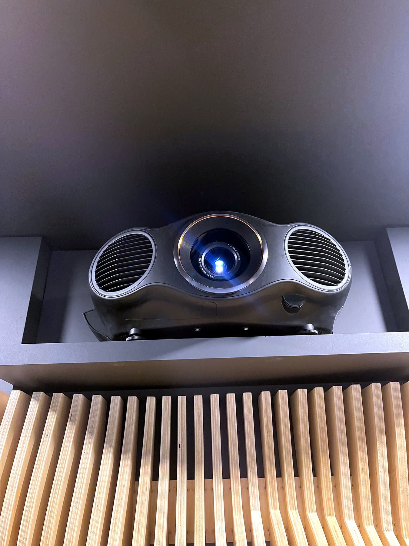 A projector set into a ceiling pocket above a slatted wood acoustic soffit