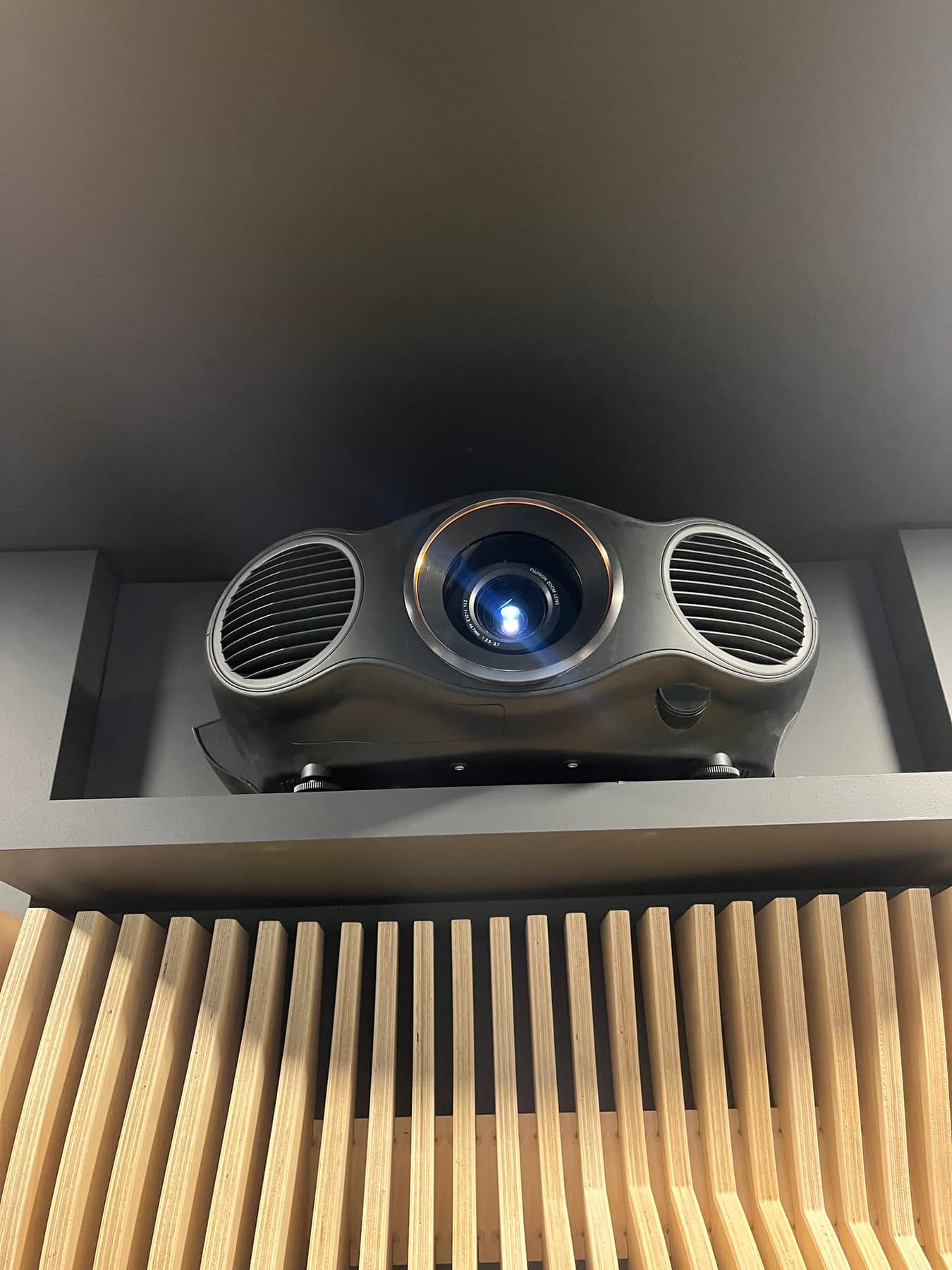 A projector set into a ceiling pocket above a slatted wood acoustic soffit